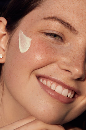 girl with freckles smiling with moisturizer on her cheek