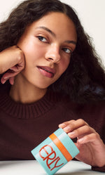 Model in brown sweater holding ERLY Start Moisturizer with SPF 40