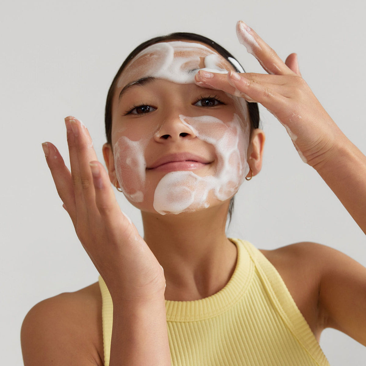 Woman applying ERLY Face Foam with a neutral background