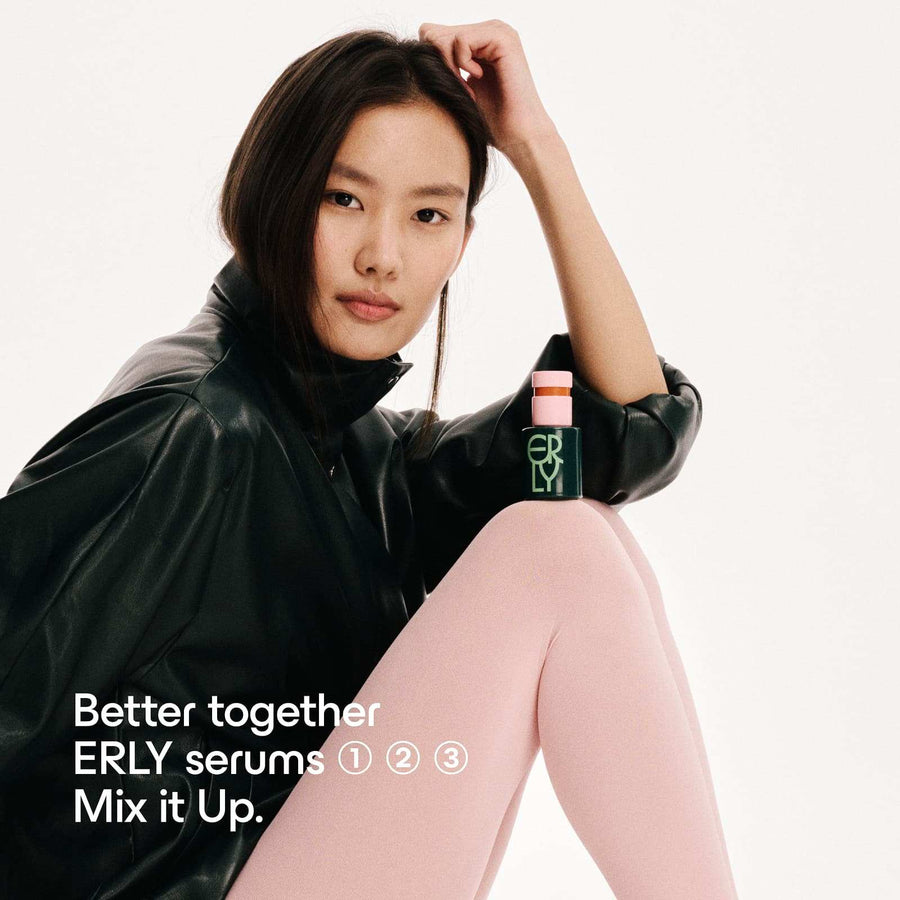 Model seated in a black jacket with ERLY Daily Soothe Serum bottle resting on her knee