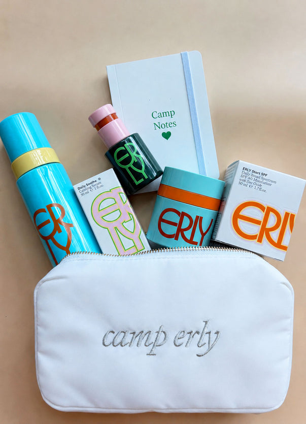 Collection of cosmetic products and 'camp erly' pouch on a beige background