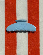 Light blue hair clip with 'ERLY' branding on a orange and white striped background