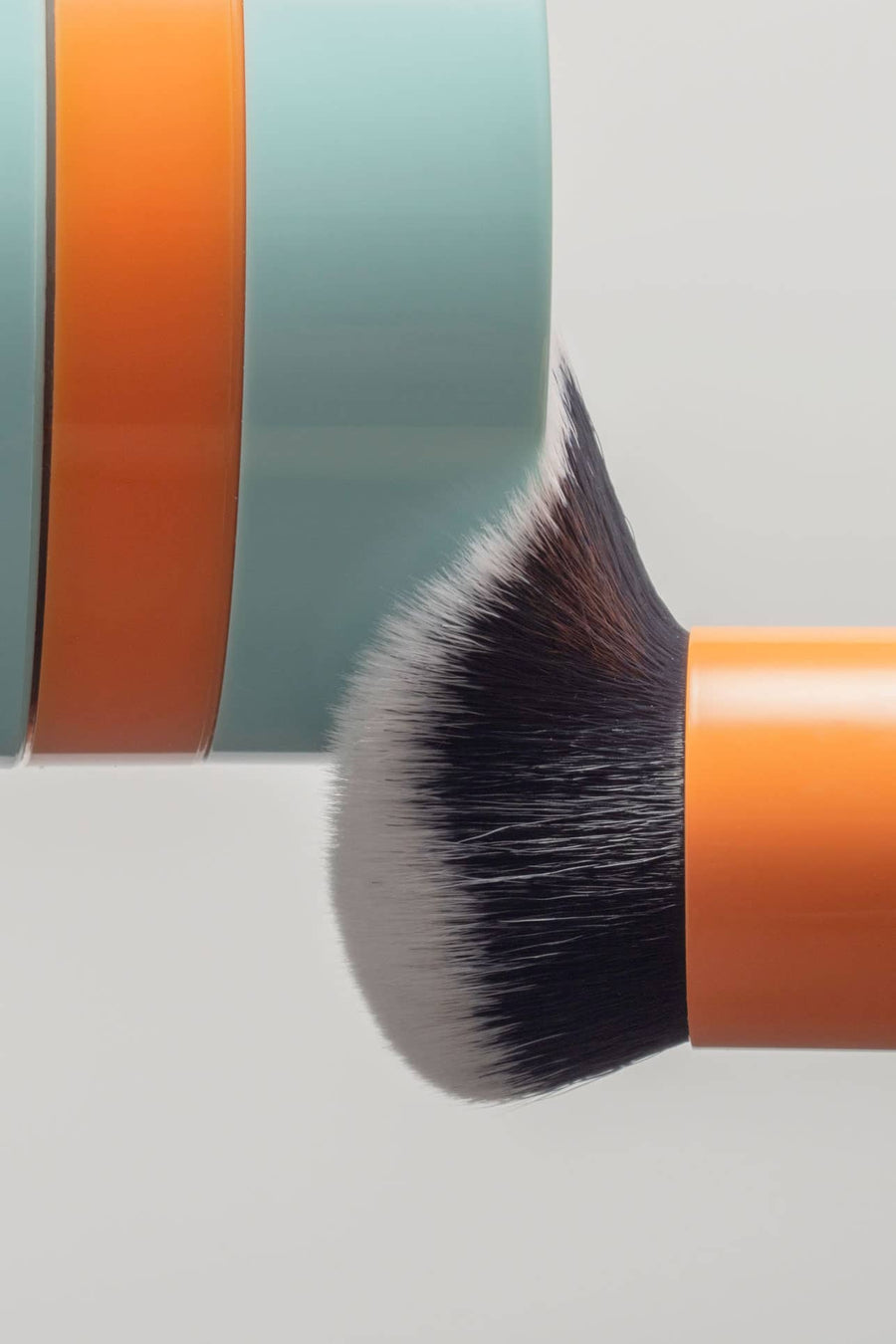 Makeup brush with orange handle and gray bristles on a light gray background