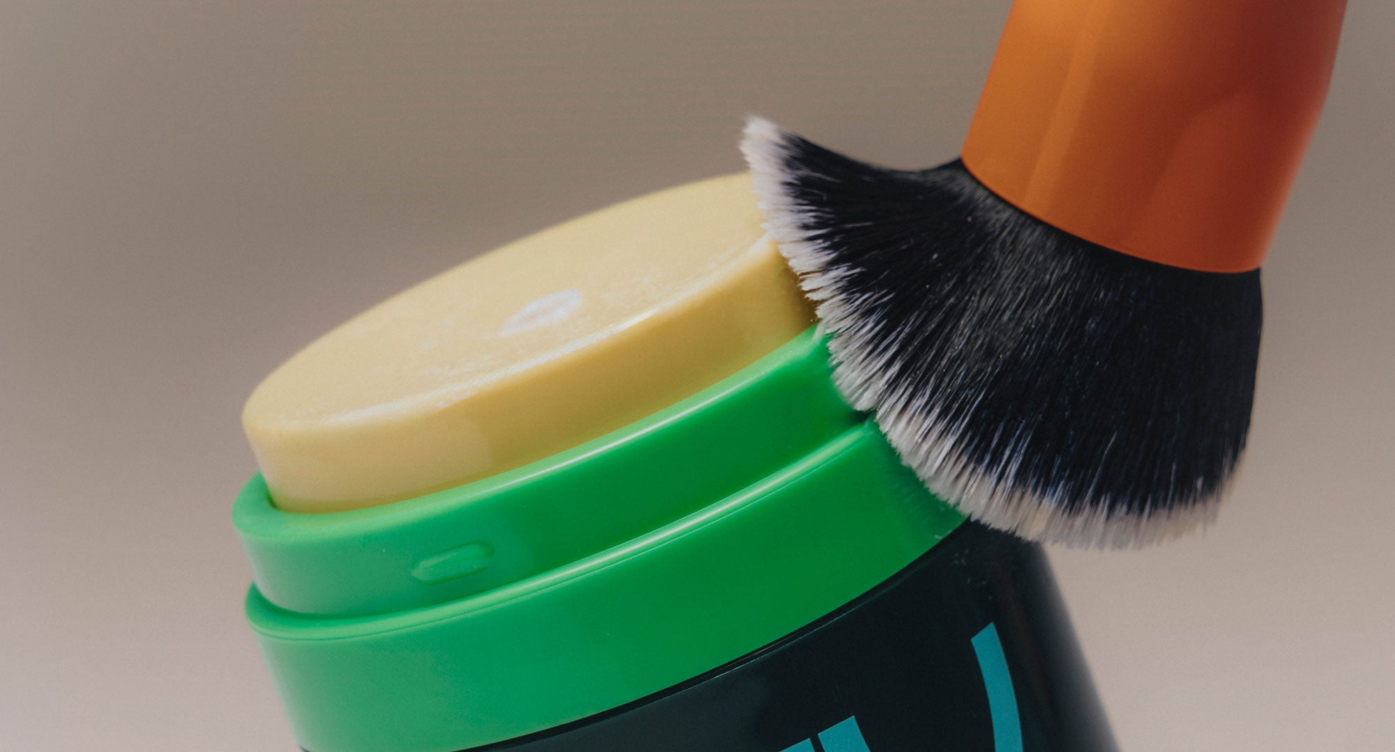 Green container with a yellow lid and black brush on a beige background