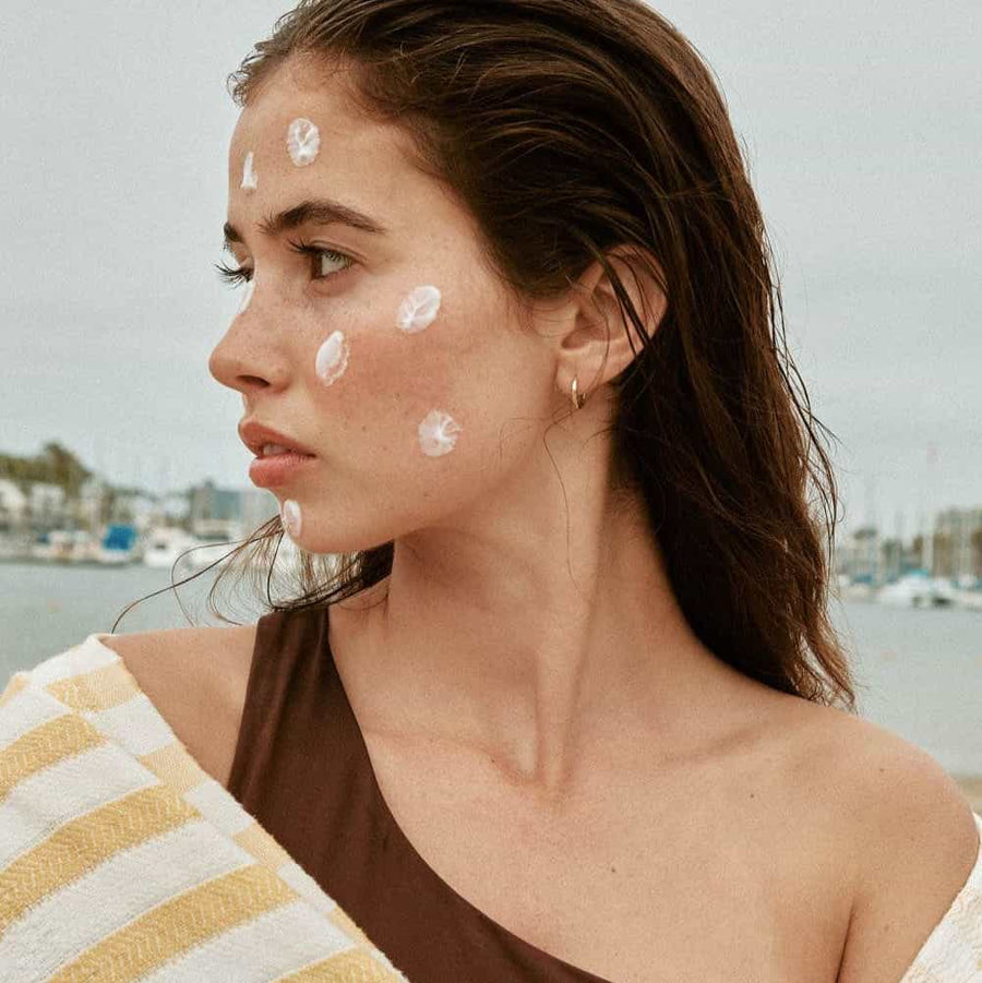 model in striped towel with sunscreen on her face and wet hair 