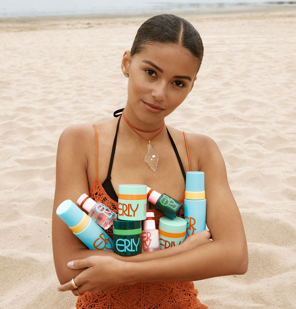 model in bathing suit on the beach holding the erly routine products